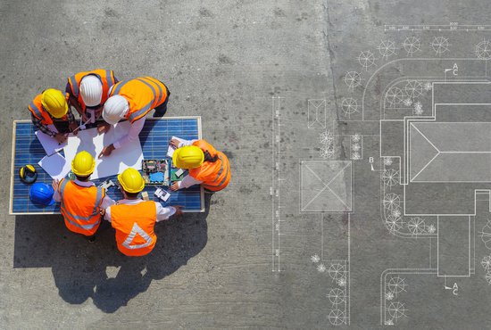 Top view of architectural engineer working on his blueprints with documents on construction site.
